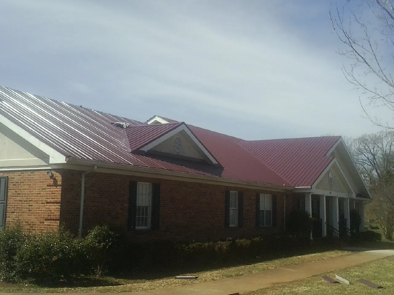 Red metal roof with gabled entries on a long brick building, from a Hail Damage Roof Repair job in Rockdale