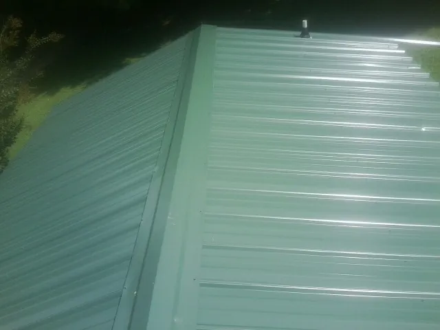 New green metal panels meeting at the ridge of a roof — Flat Roof Repair work by our crew in Rockdale