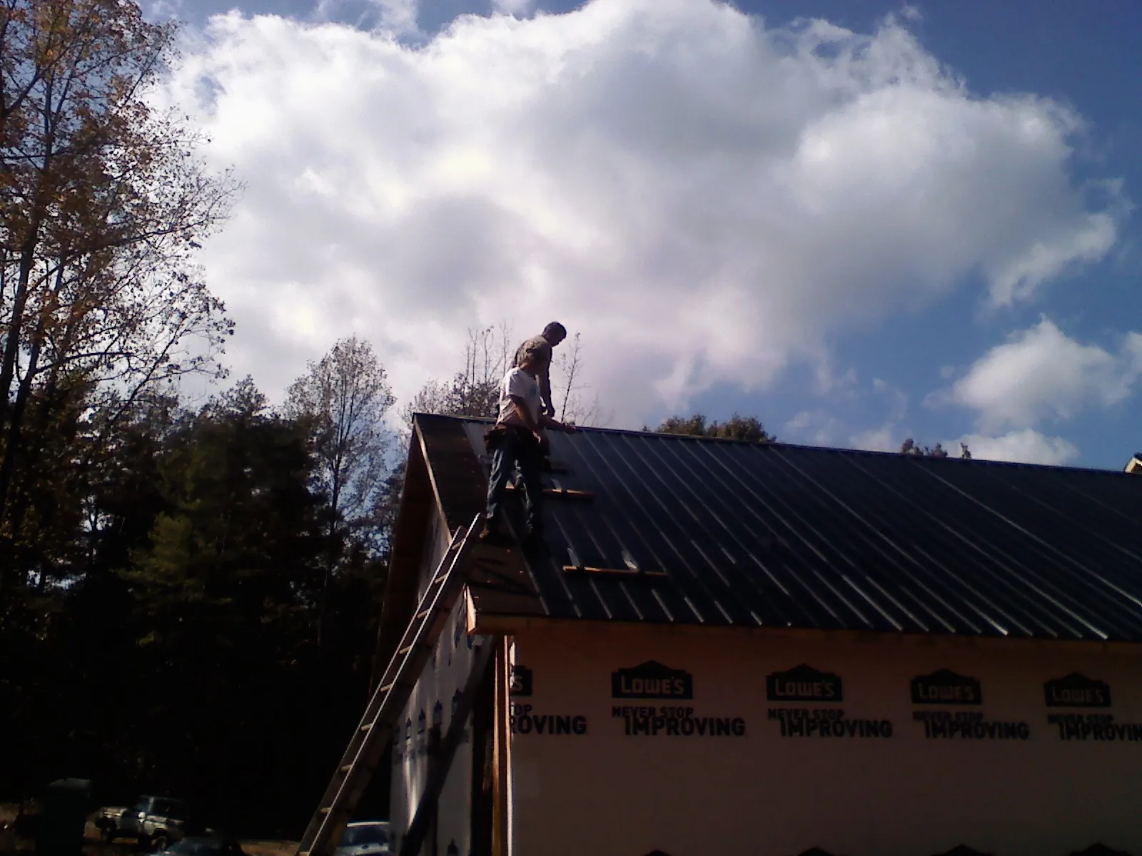 Roofer fastening dark metal panels high against a cloudy sky, from a Roof Inspection job in Rockdale