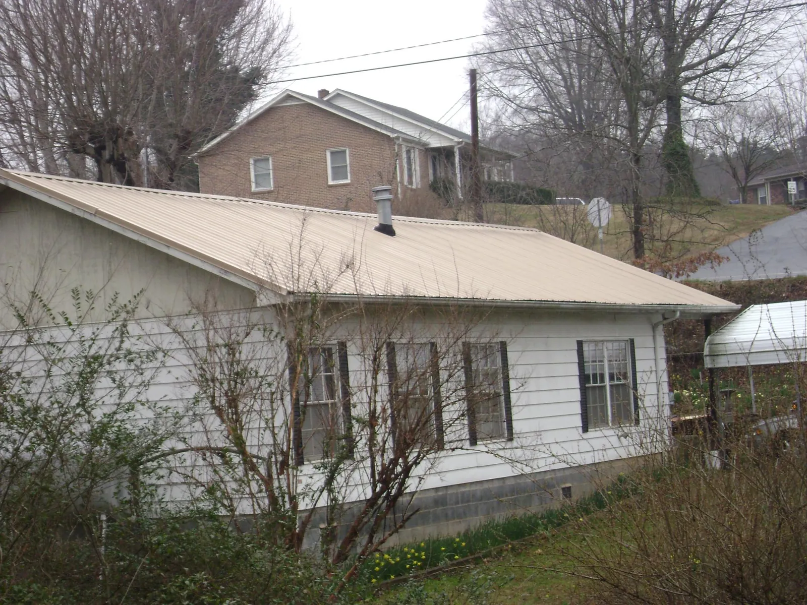 Tan metal roof on a white sided house set into a hillside — Commercial Roofing by Roofing Brothers in Rockdale