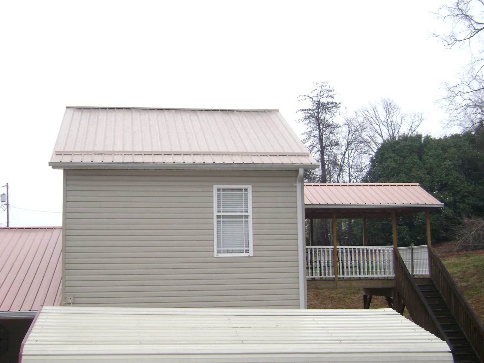 Tan metal roofs on a two story addition and attached porch, from a Roof Replacement job in Rockdale
